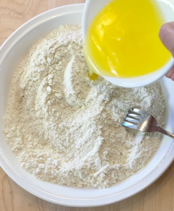Pouring melted butter into pie pan with flour, salt, sugar, and fork for mixing.