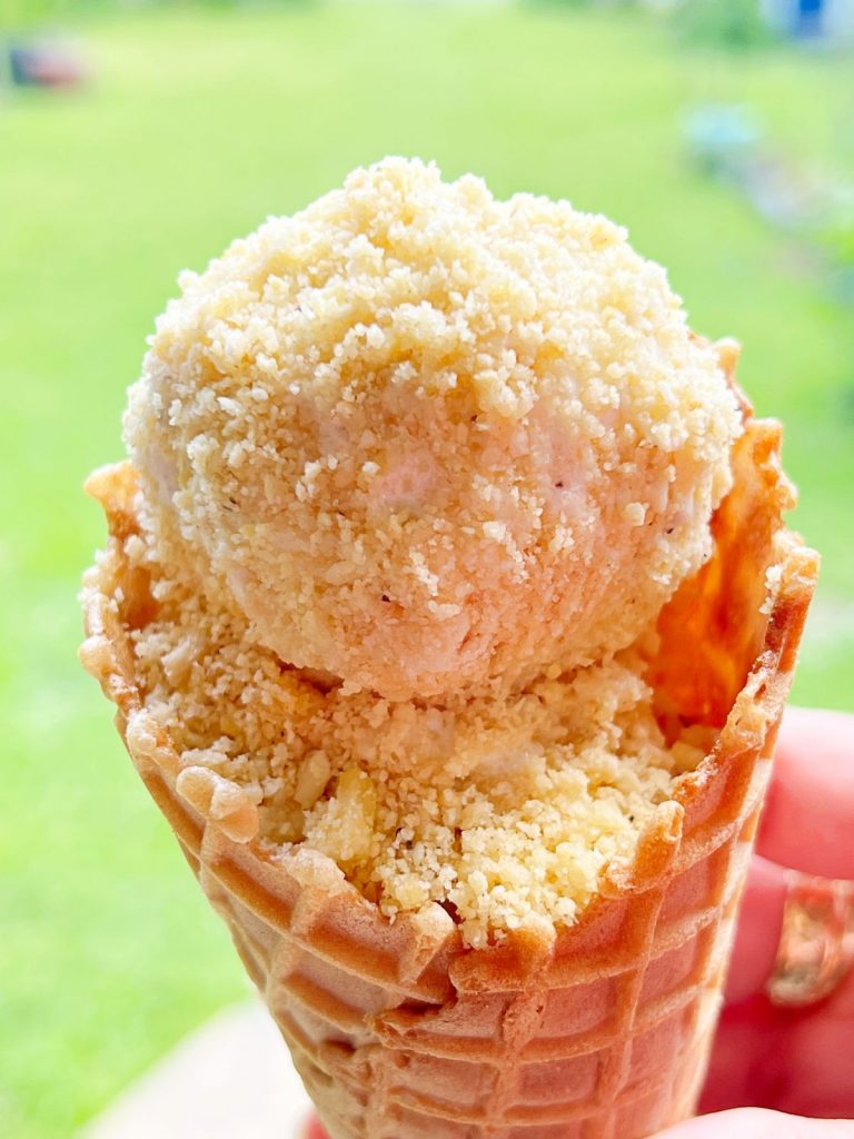 Close up ice cream cone with vanilla scoops of ice cream covered in banana pudding crunch topping.
