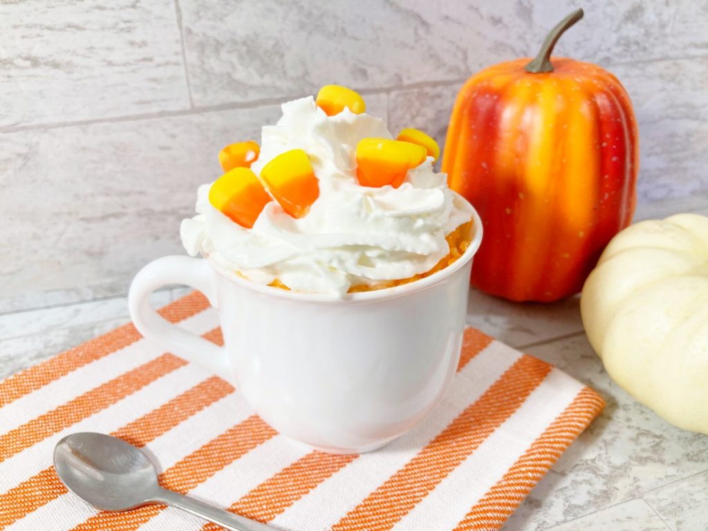 finished candy corn cake in a mug next to white and organge pumpkins.