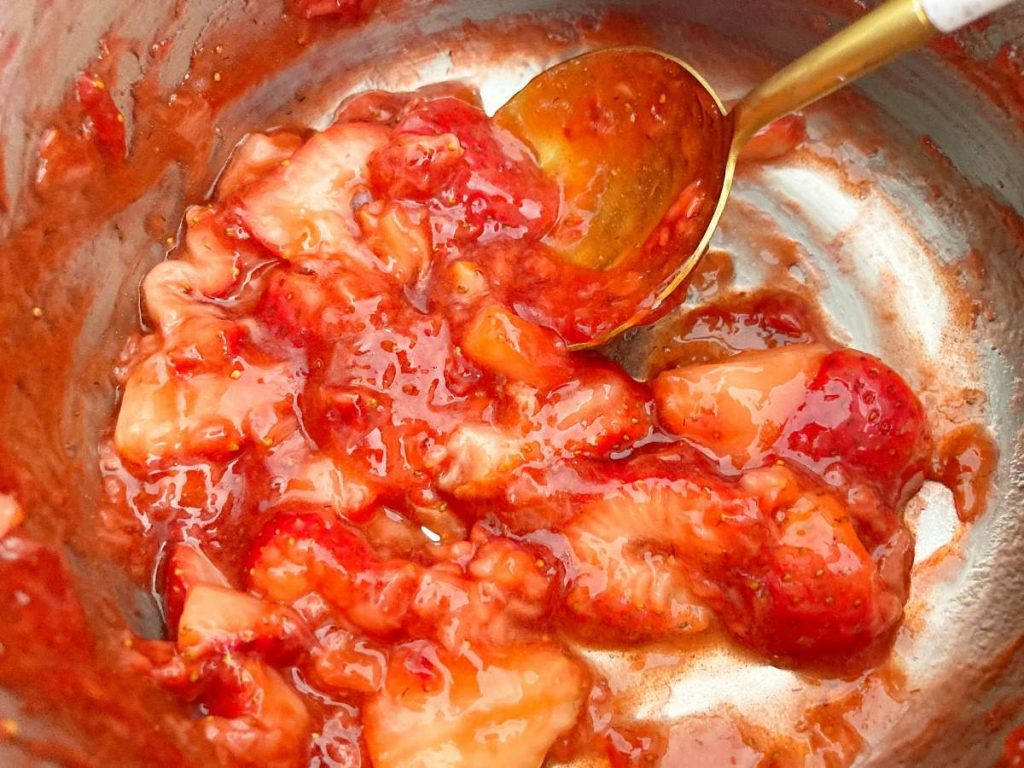 cooked strawberry sauce in saucepan with gold spoon.