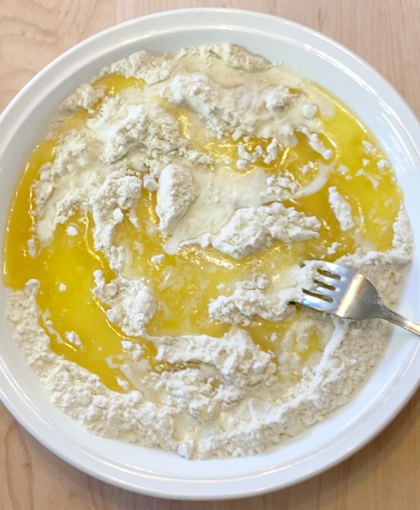 White pie pan with flour mixture, melted butter an fork.