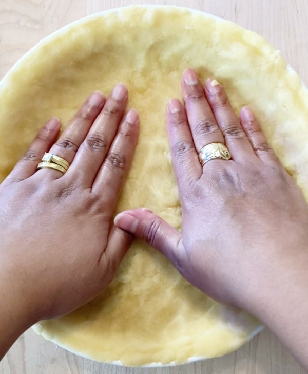 Pressing pie crust dough into pie pan with hands.