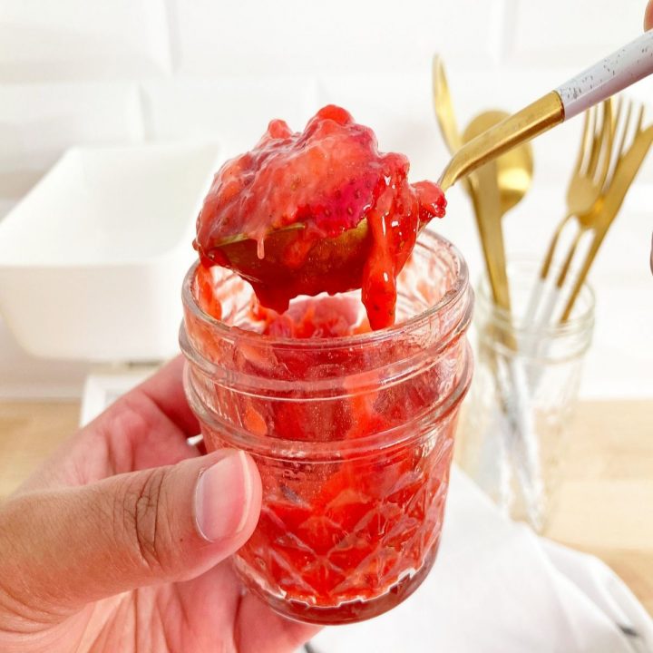 Strawberry sauce in small mason jar with some of the sauce on gold spoon.