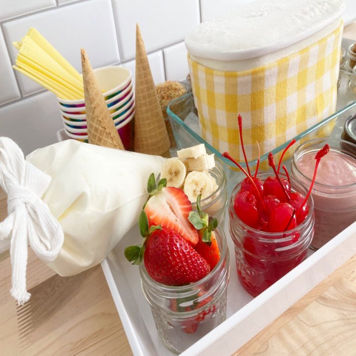 White tray with vanilla ice cream, sliced strawberries, sliced bananas, whipped cream, cherries and cones.