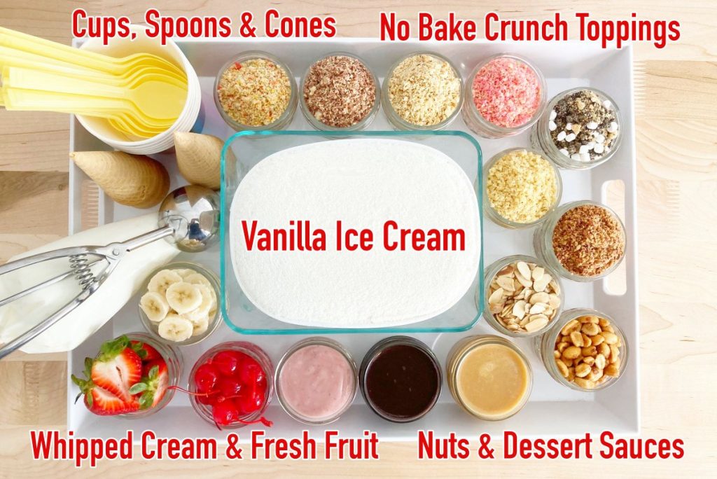 White tray with vanilla ice cream, good humor inspired crumble toppings, dessert sauces, fresh fruit, nuts, ice cream scoop, cones, cups, yellow plastic spoons, and whipped cream.