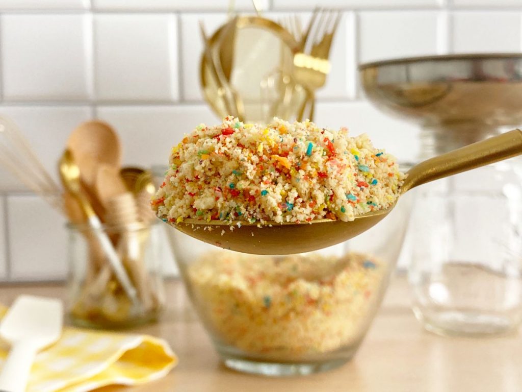 Spoonfull of finished funfetti birthday cake crumble. Gold and white spoon with bowl of crunch in background.