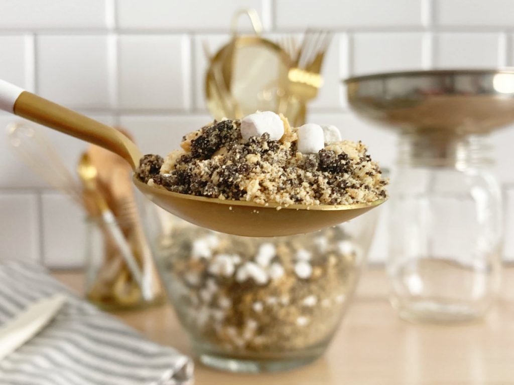 Spoonfull of finished s'more crumble. Gold and white spoon with bowl of crunch in background.