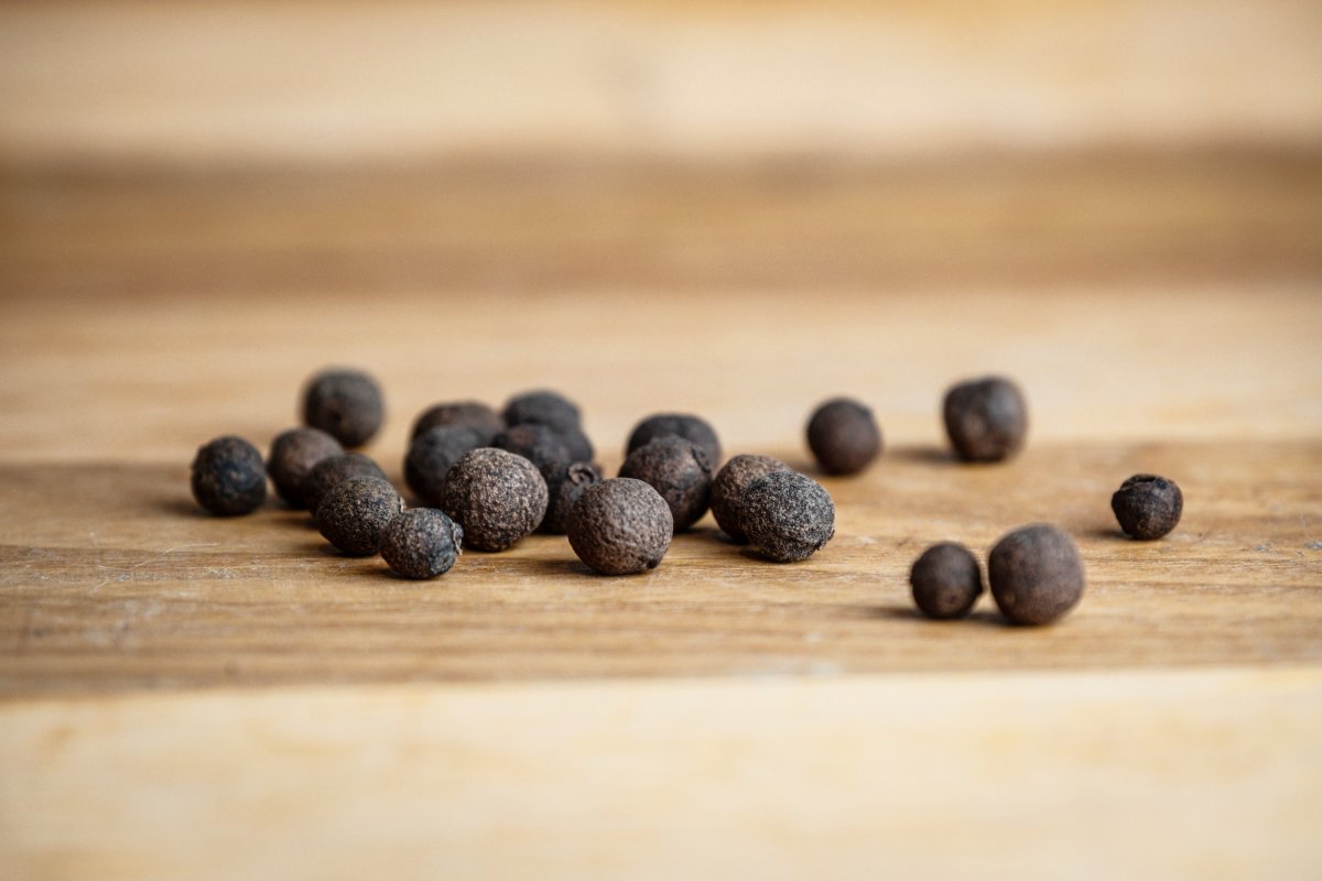 A pile of allspice berries on wood countertop.
