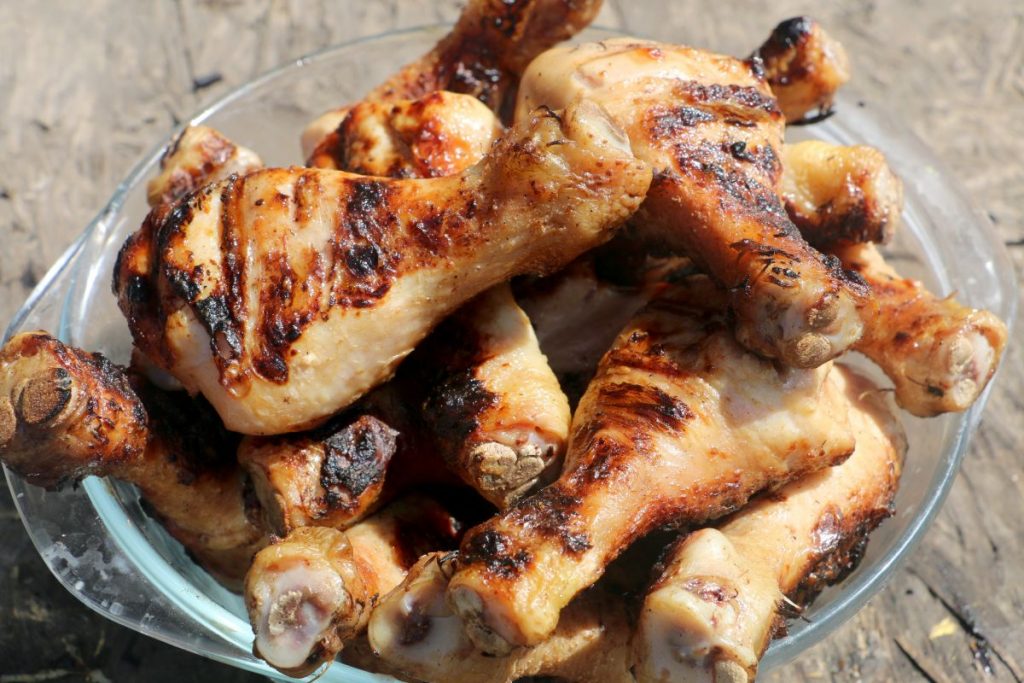 Large glass bowl filled with roasted chicken drumsticks. Perfect cheap food to buy when you're broke.
