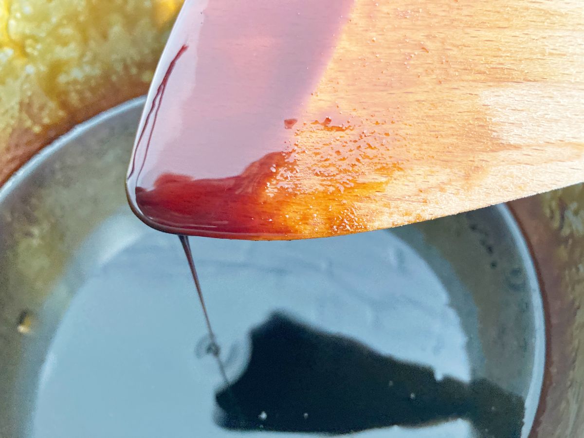 Slightly thickened browning sauce in saucepan dripping from wood spatula.