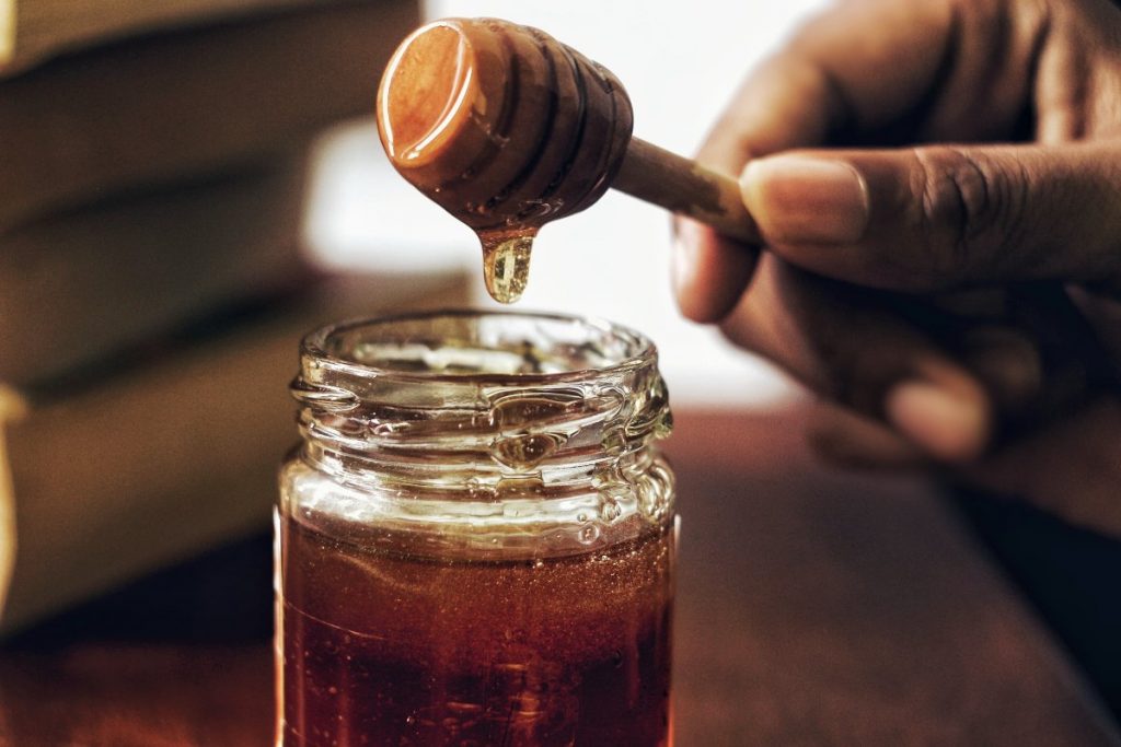 Hand holding a honey dipper and a small bottle filled with honey.