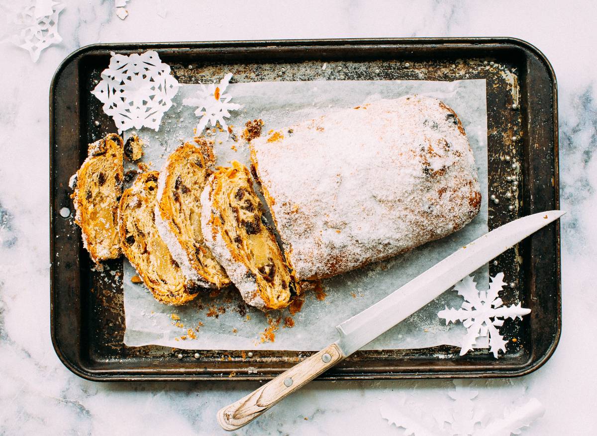 Sliced christmas stollen bread on metal tray with knife. Paper snowflakes around bread.