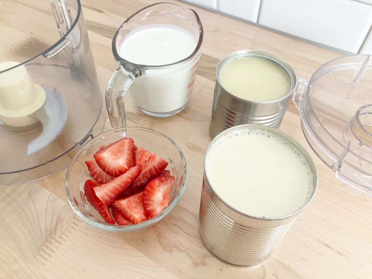 Strawberry leche milk mixture ingredients next to food processor bowl and lid.