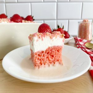 Slice of strawberry crunch tres leche cake on a white plate topped with a fresh strawberry.