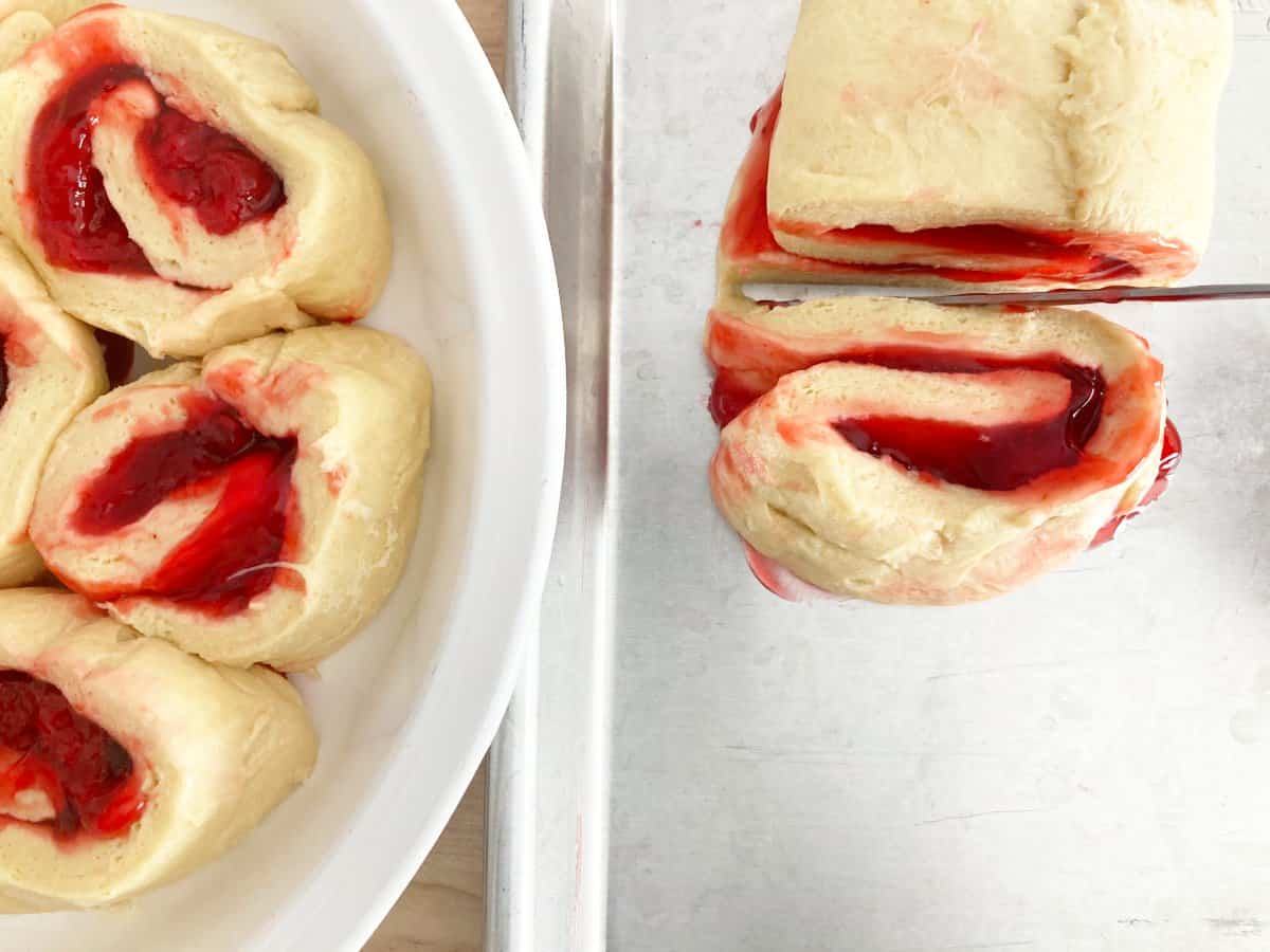 Knife cutting unbaked strawberry roll into 2 inch pieces.