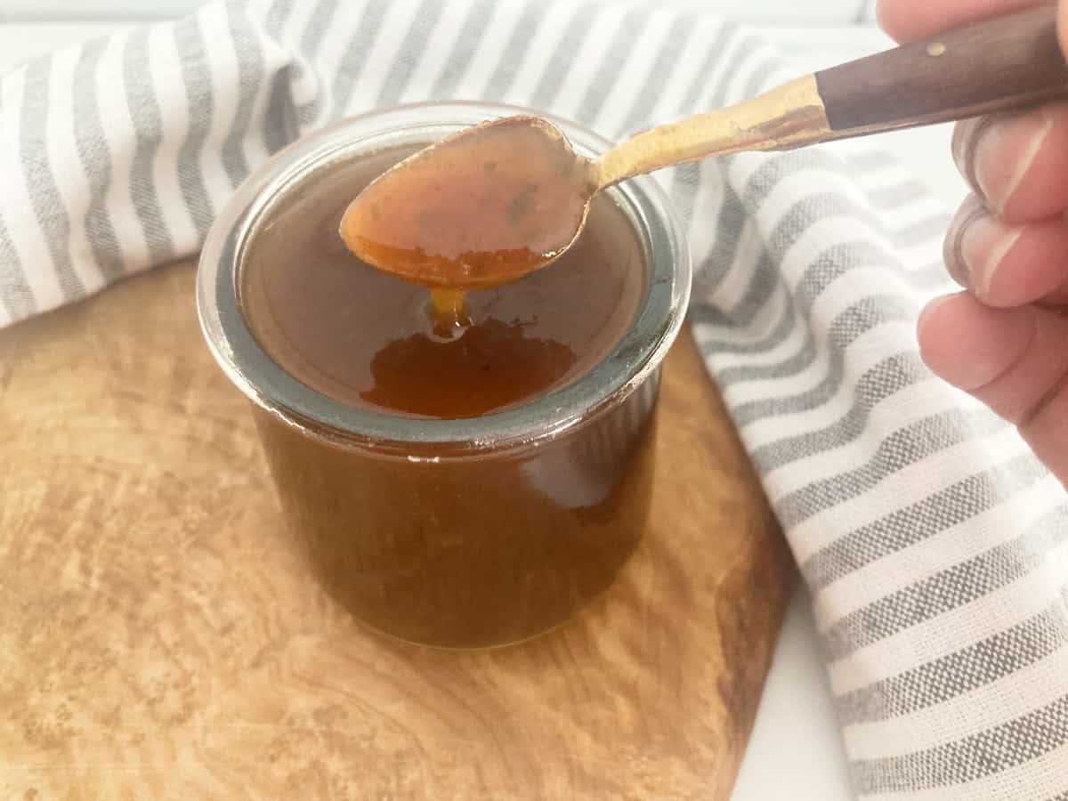 Tamarind chutney in a glass jar. Hand using a gold spoon to show it's texture.