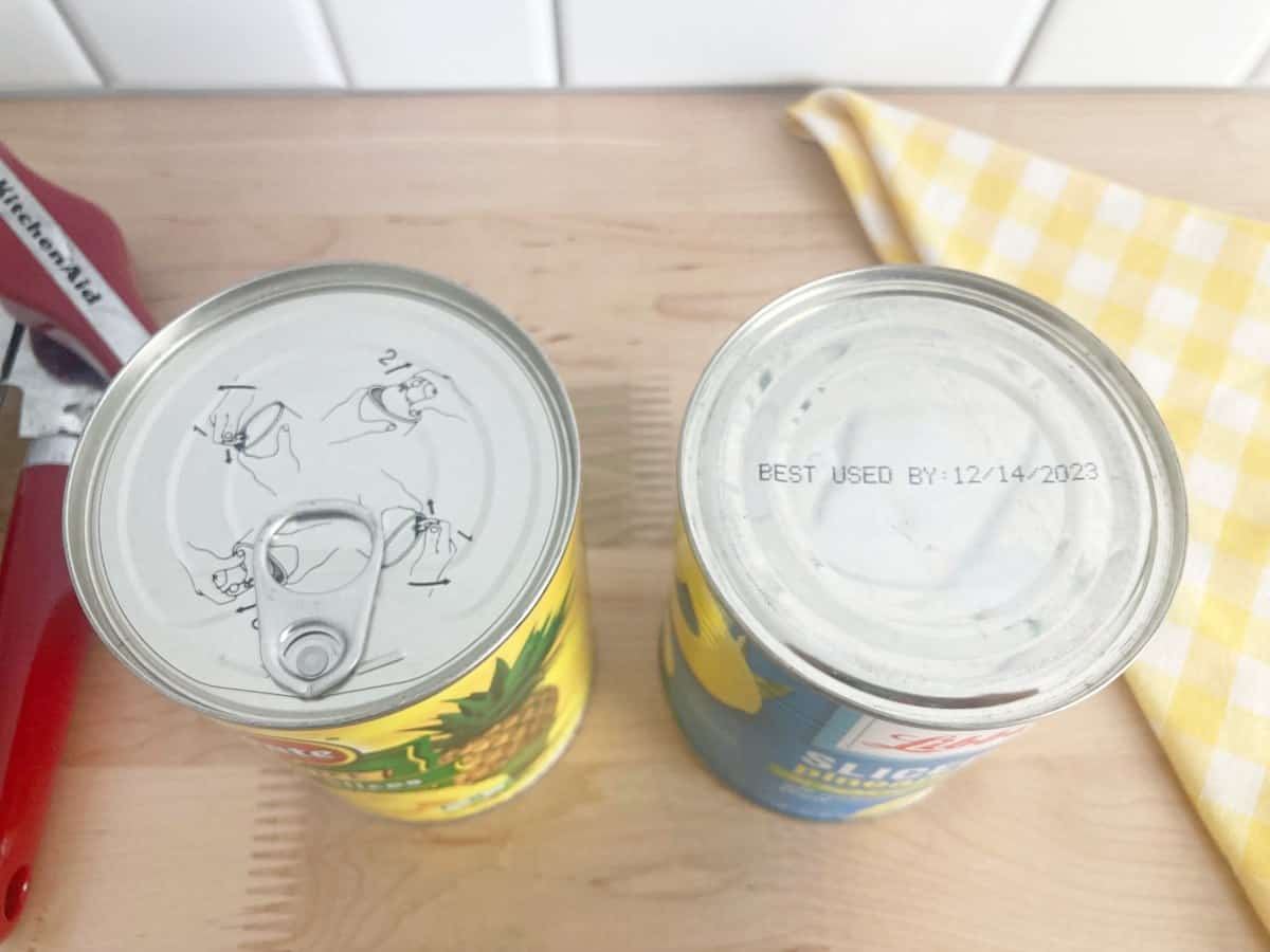 Top down view to two cans of unopened canned pineapple. One showing the best by date of 12/14/23.