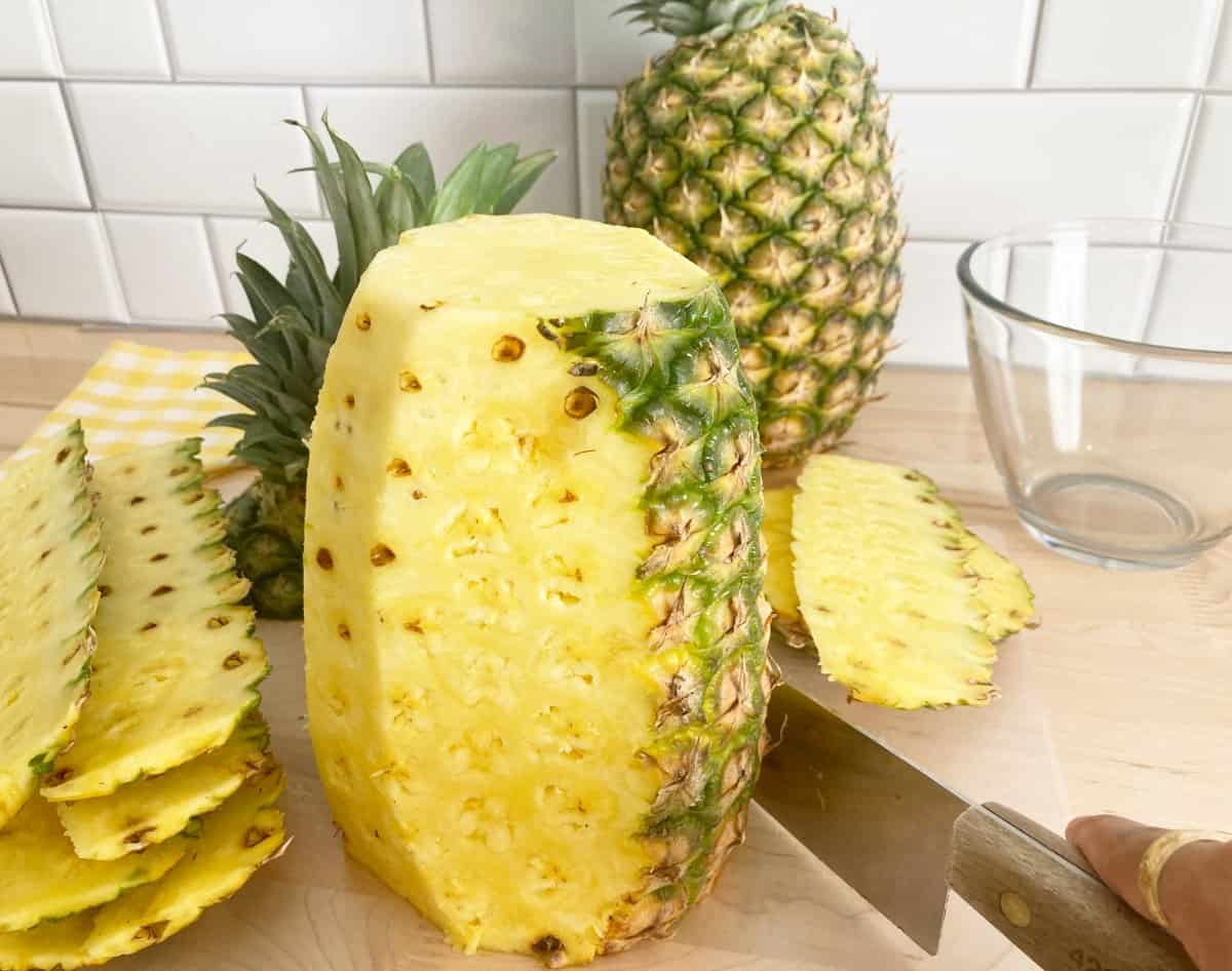 Hands cutting the skin of fresh pineapple with a knife.