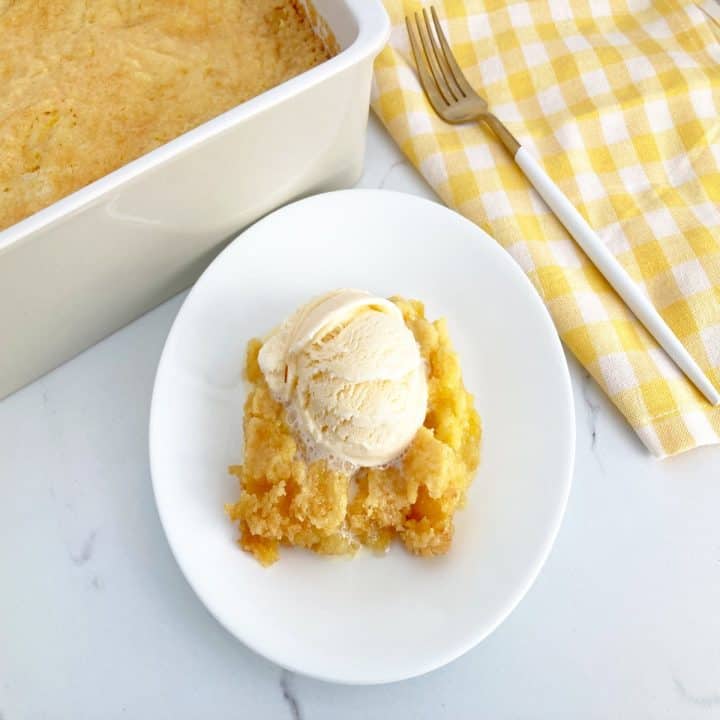 Baked pineapple dump cake topped with ice cream on a white plate. Next to baking pan with the finished cake.