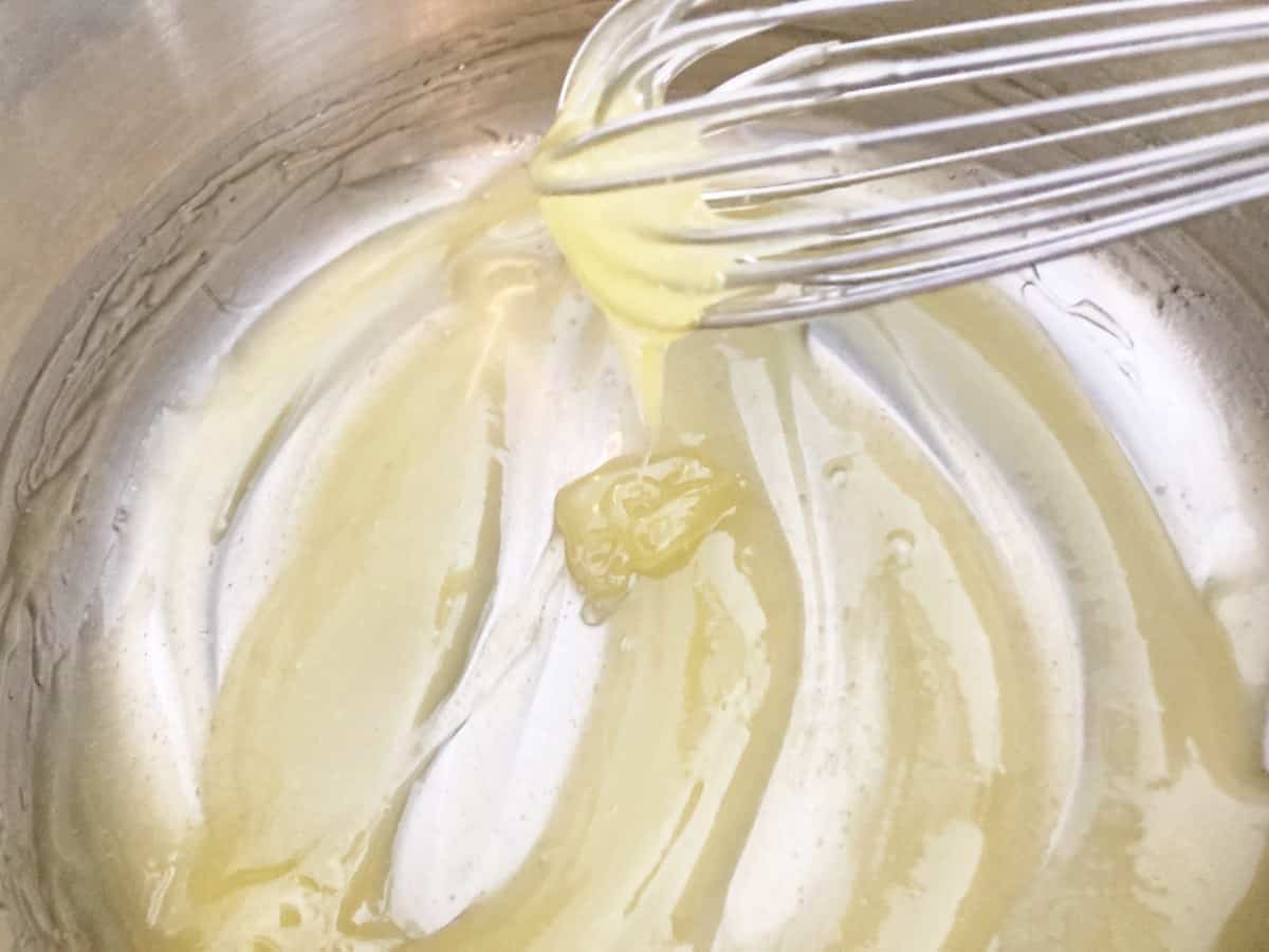 Thickened pineapple sauce dripping from a silver whisk, showing the texture.