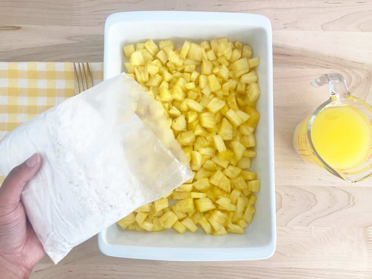 With hands topping the tidbits with pineapple cake mix.