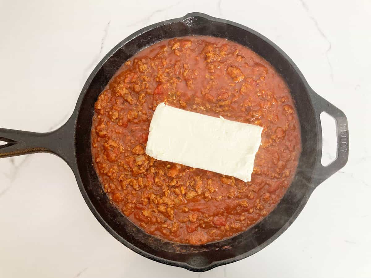 A block of cream cheese added to the pasta sauce with the ground beef.