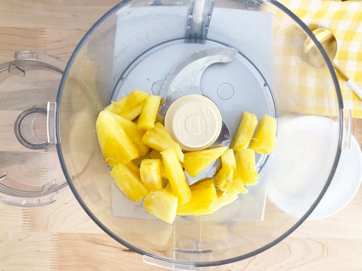 Fresh pineapple tidbits are added to the food processor bowl.