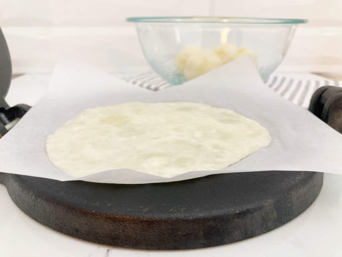 Flattened cassava tortilla dough on the tortilla press with parchment paper.
