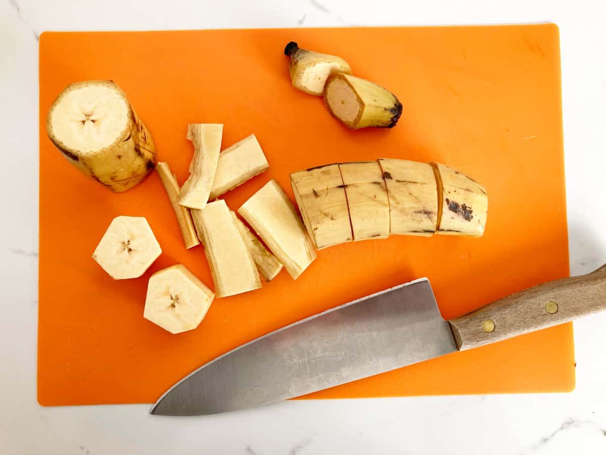 Cutting fresh plantain int slices on a orange cutting board.
