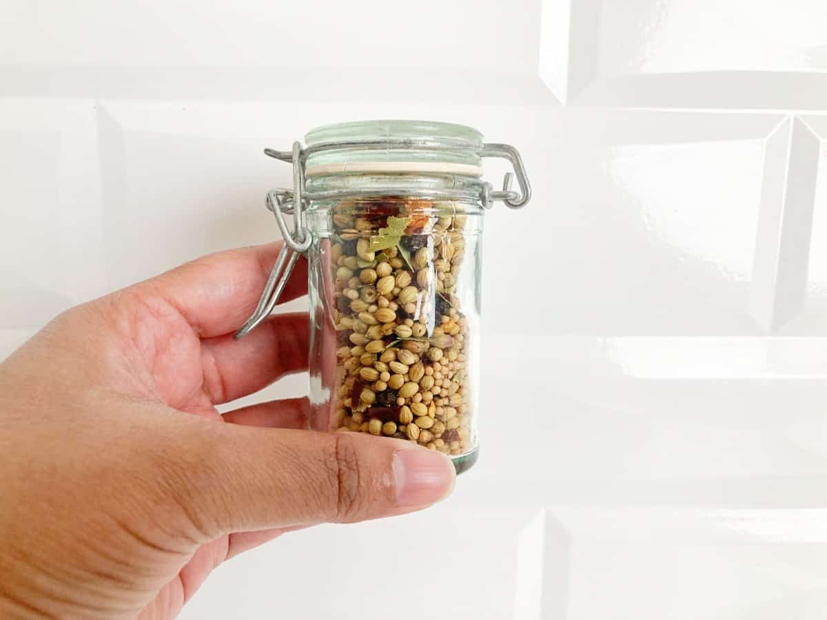 Hand holding glass spice bottle filled with corned beef spice blend.