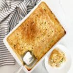 Homemade chicken cobbler with a serving removed with a spatula. Next to a plate with a serving of casserole and a white and grey towel.