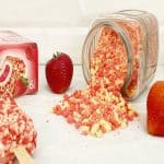 Strawberry shortcake crumble pouring out of a glass jar. Next to a box of good humor shortcake ice cream bars, an opened dessert bar and fresh whole strawberries.