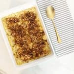 Baked no peek chicken in a white baking dish. Next to a gold serving spoon and grey white kitchen towel.