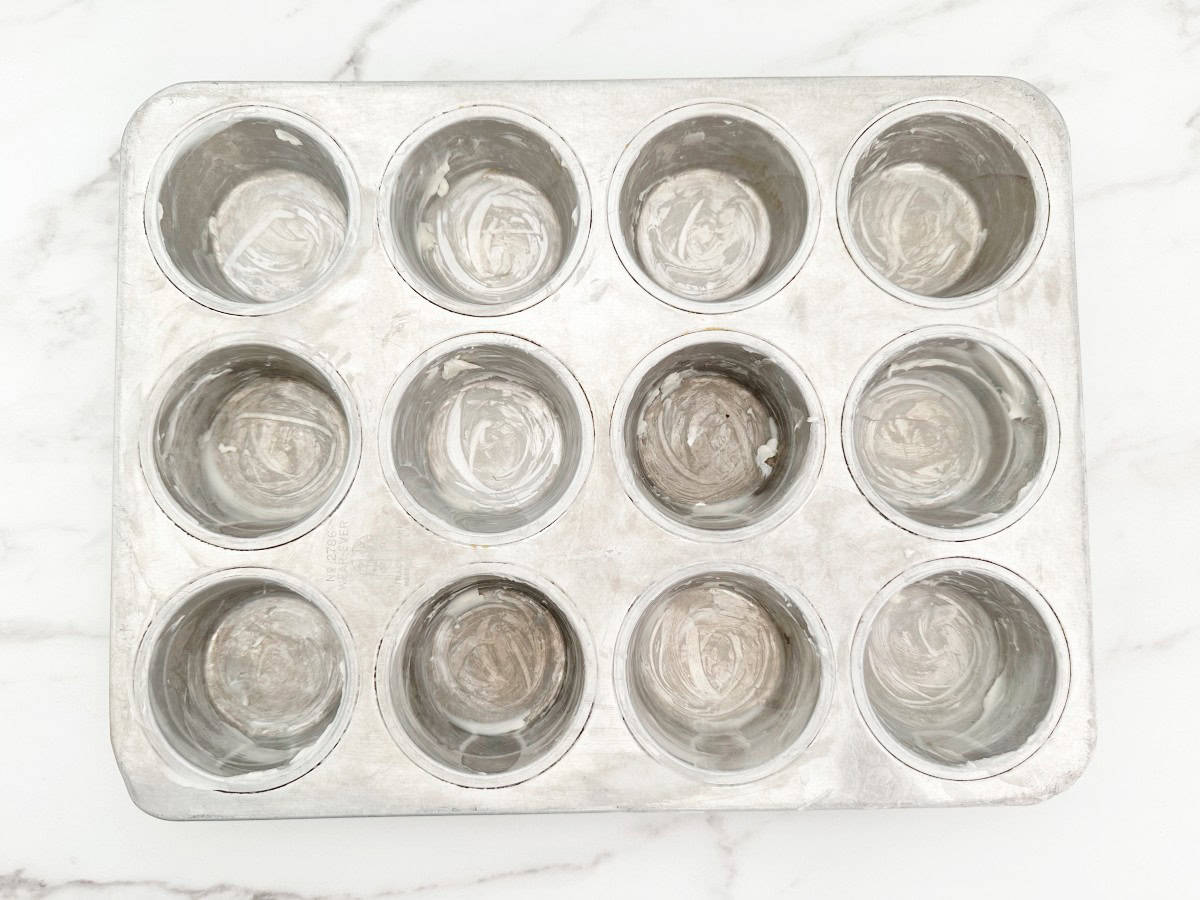 Down view of buttered silver muffin pan.