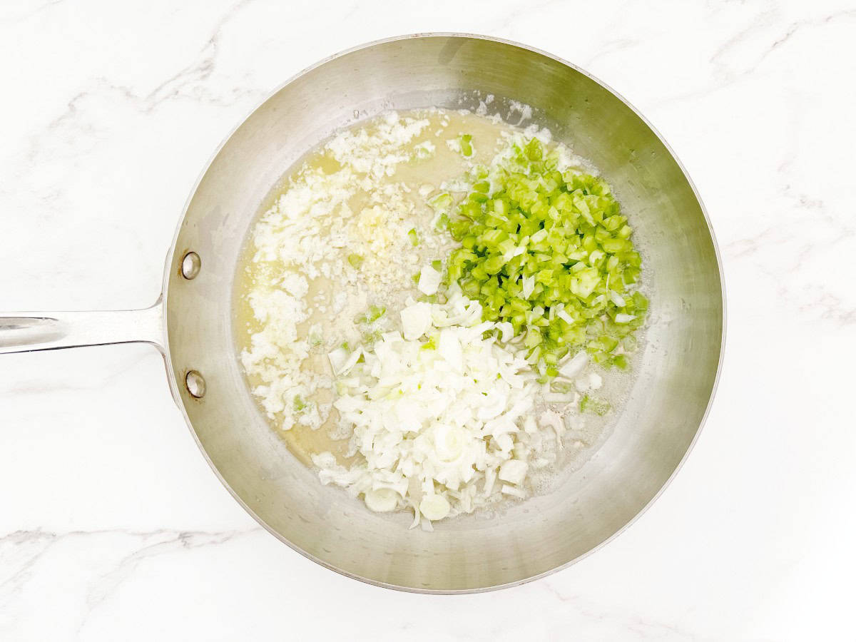 Down view silver skillet with cooking butter, garlic, onion and celery.