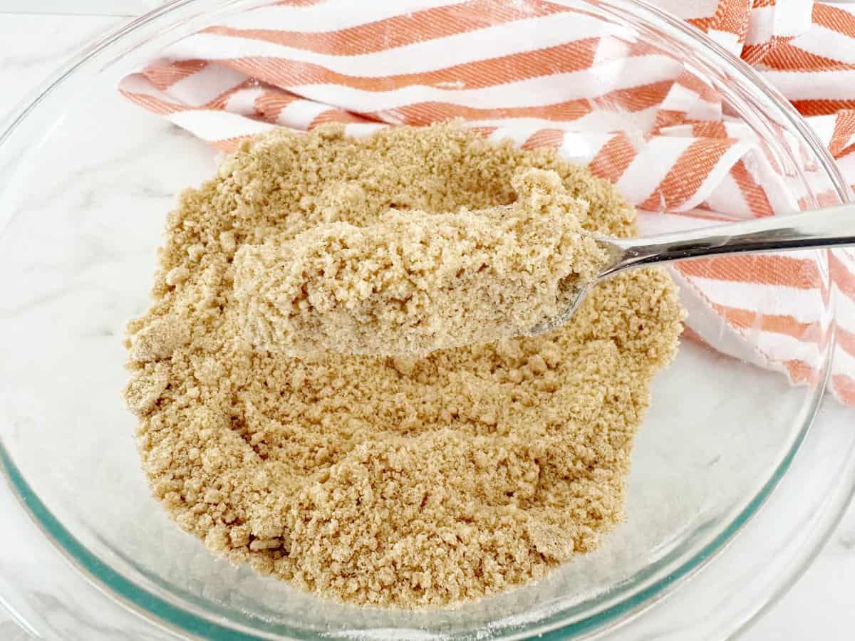 Finished crumble topping in clear bowl with silver fork.