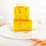 White plate with two pieces of jiffy pumpkin cornbread stacked on each other. Topped with butter and drizzled honey.