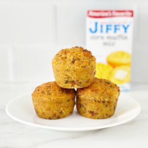 Three jiffy cornbread stuffing muffins on white plate. Next to a jiffy corn muffin mix.