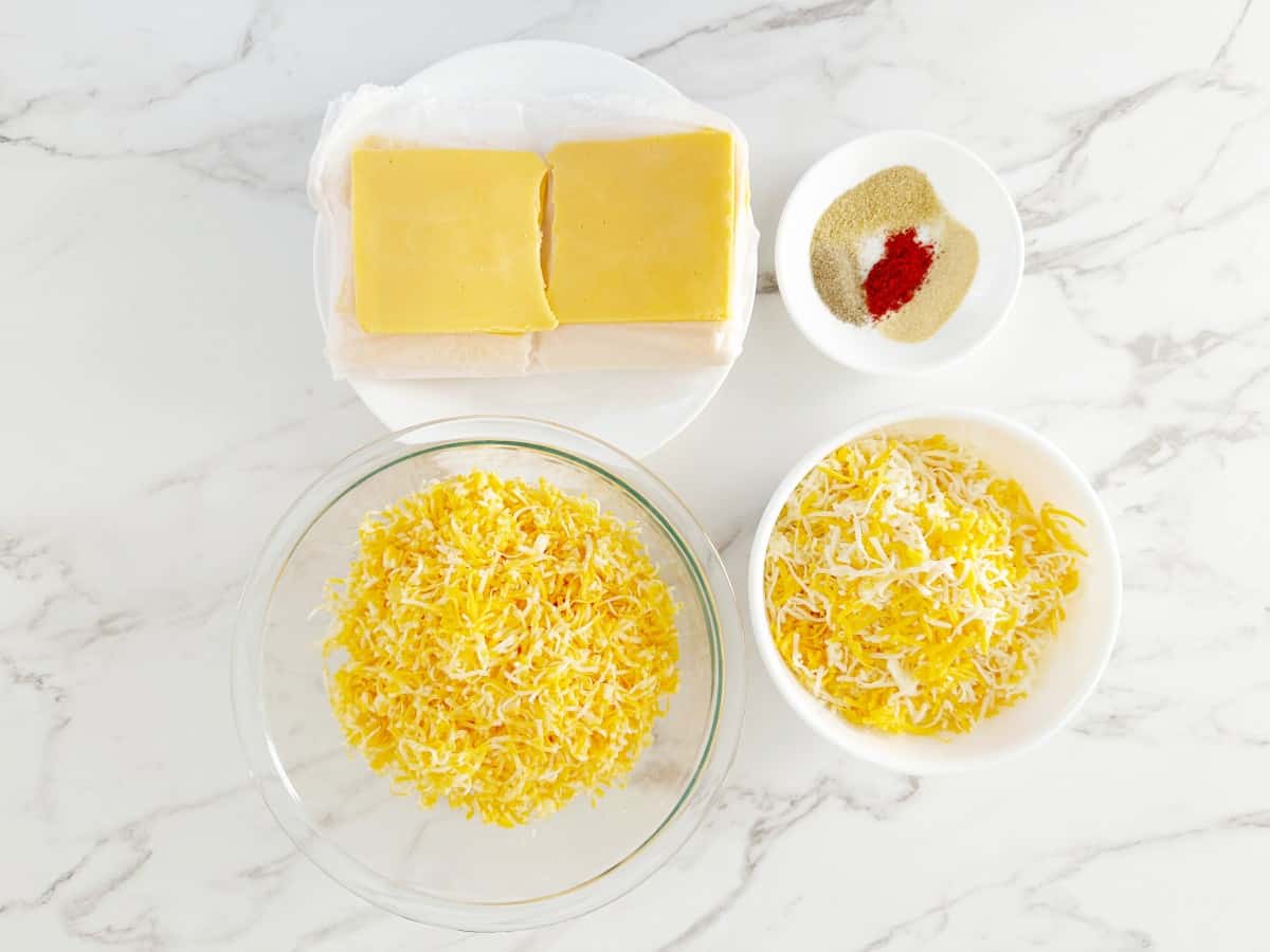 Down view of prepped cheeses in bowls, sliced American cheese and plate with spices.