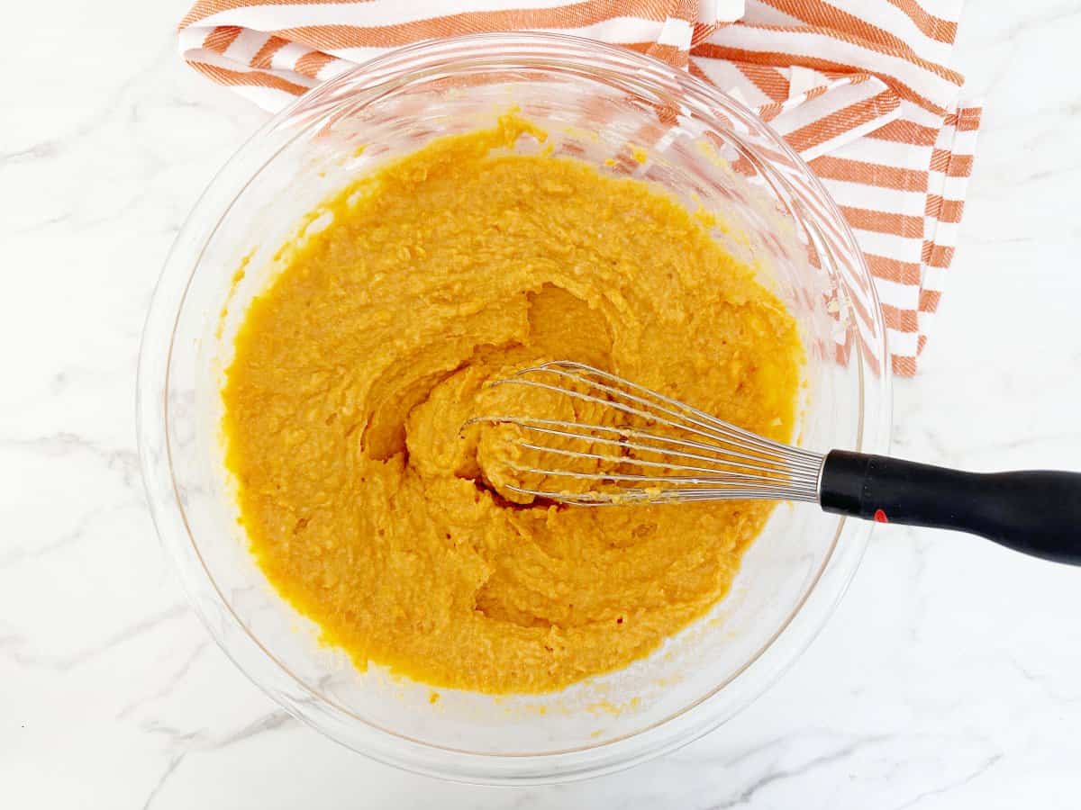 Down view sweet potato mixture in clear bowl with wire whisk.