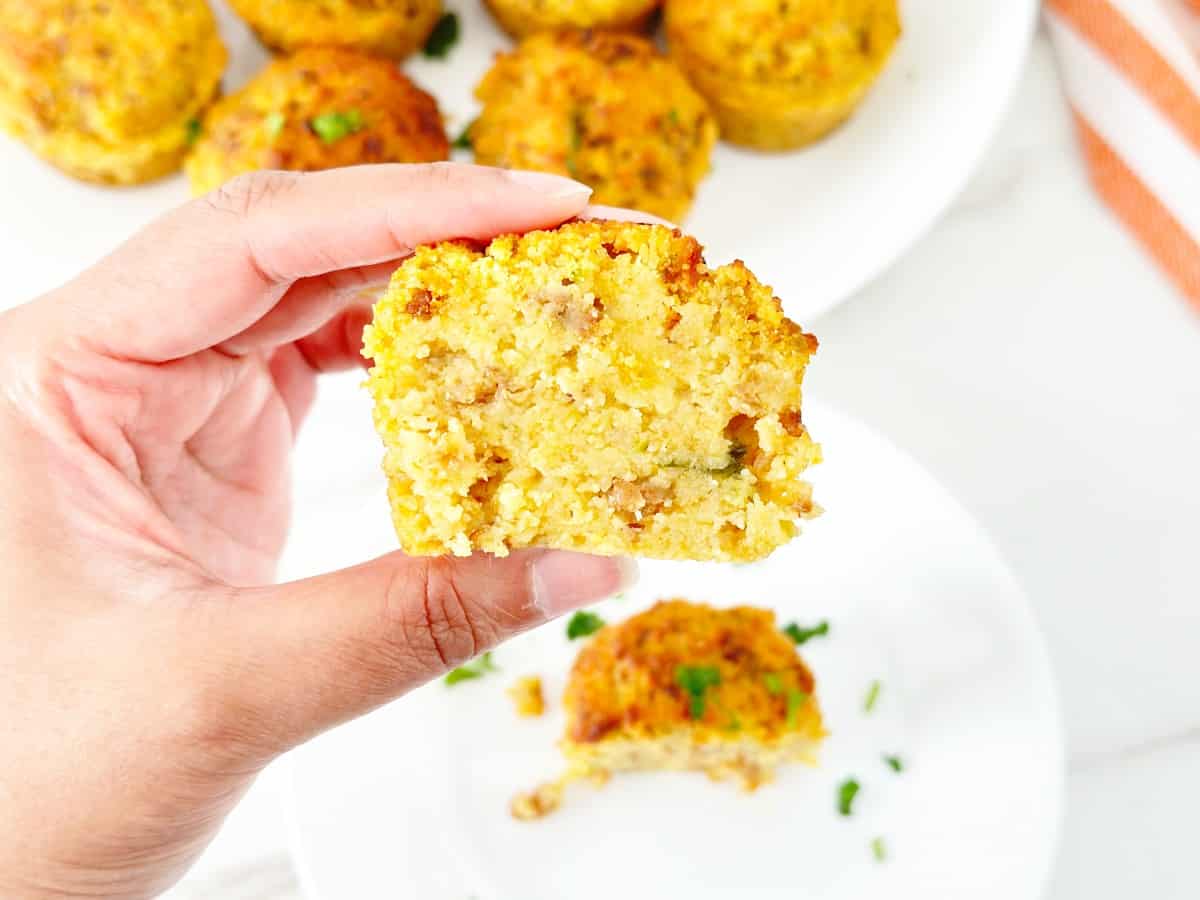 Hand holding a cut piece of cornbread stuffing muffin. Shows inside texture.