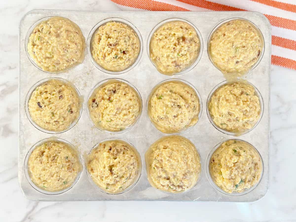 Unbaked cornbread stuffing muffins in silver muffin pan.