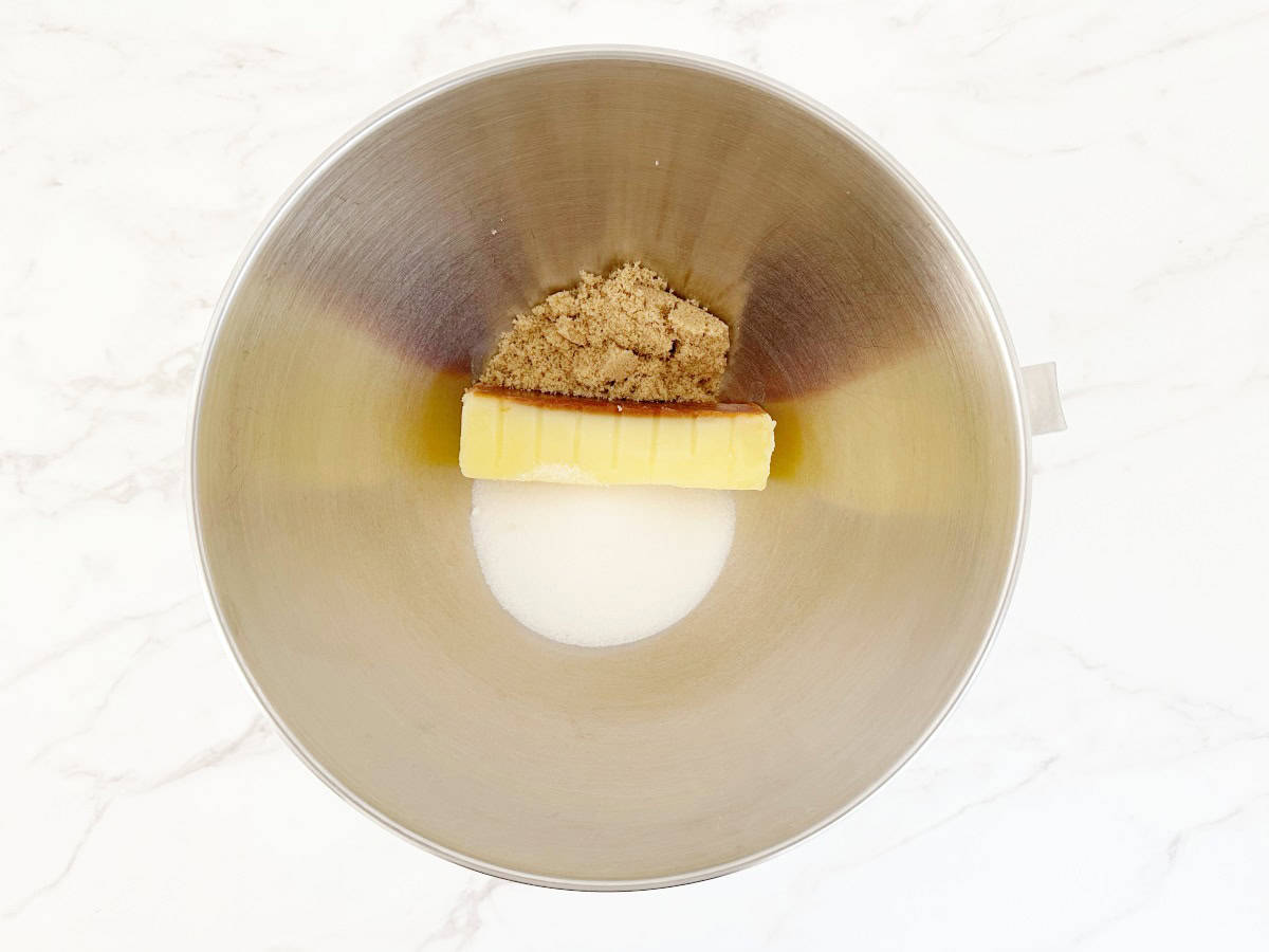 Down view of stick of butter, granulated sugar and brown sugar in silver mixing bowl.