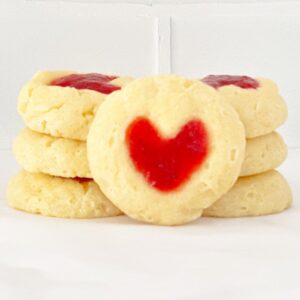 Side view of heart strawberry cheesecake thumbprint cookie with more stacked cookies behind it.