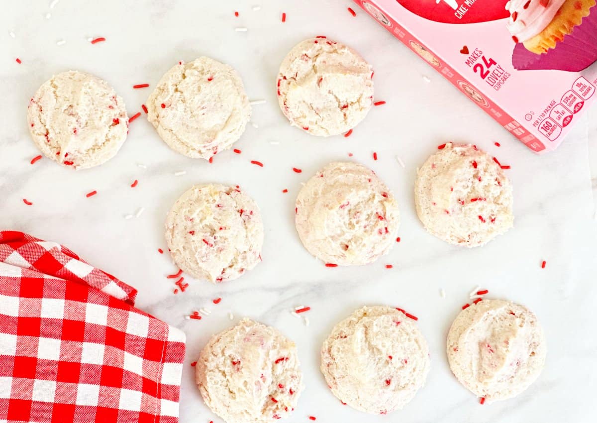 Down view of nine Valentine's Day cake mix cookies with sprinkles. New to boxed cake mix and red white checkered kitchen towel.