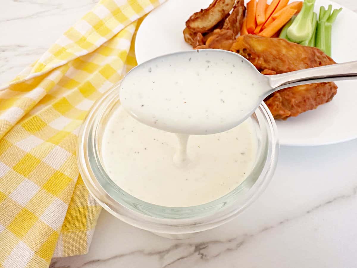Restaurant style ranch dressing dripping from a silver spoon into a jar.