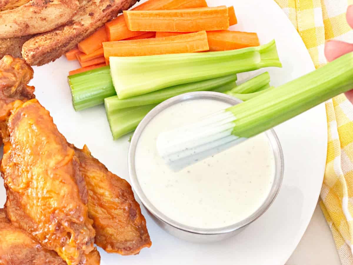 Cut celery dipping in ranch. Next to sliver cup of ranch dressing.