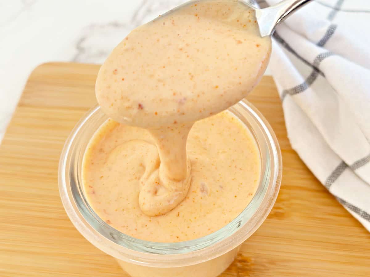 Creamy yum yum sauce dripping from a silver spoon into a jar.