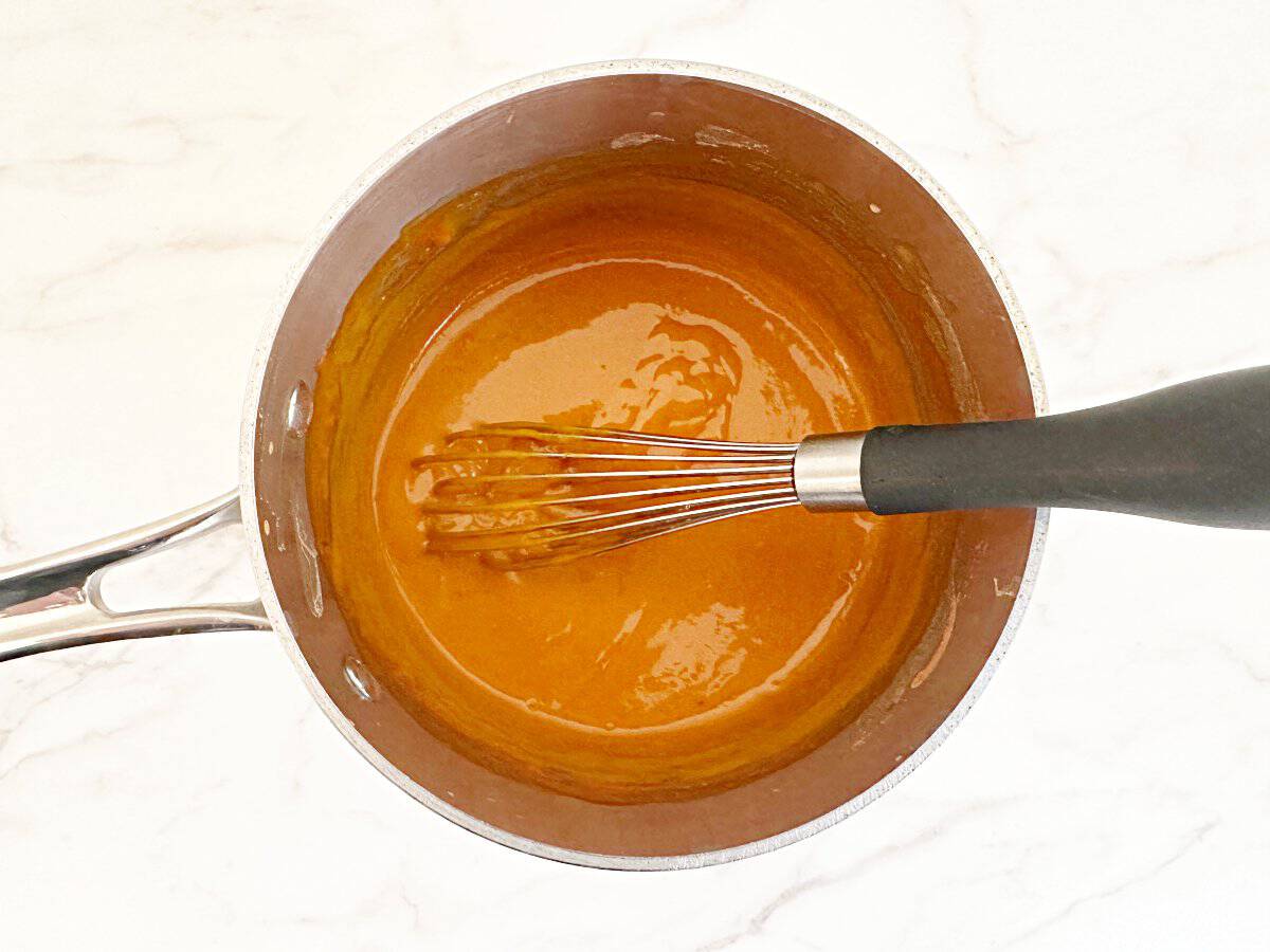 Down view of buffalo sauce in saucepan with whisk.