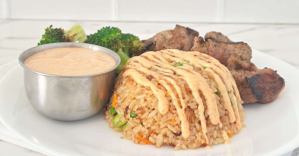 Side view of fried rice with yum yum sauce drizzled. A silver cup with more sauce on the side.